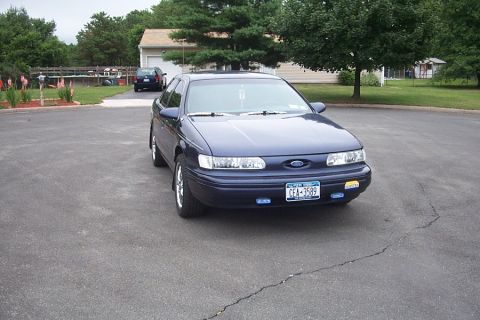1993 Ford Taurus - A 1993 Ford Taurus is parked in a suburban driveway with a garage and trees in the background.