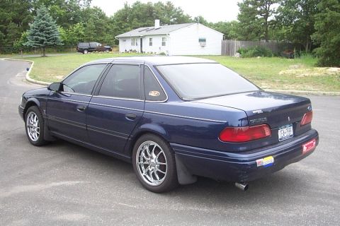 1993 Ford Taurus - This sedan is parked in a residential area with a house and trees visible in the background.
