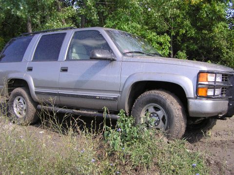 2000 Chevrolet Tahoe - Silver Chevrolet Tahoe SUV parked off-road with trees in the background.