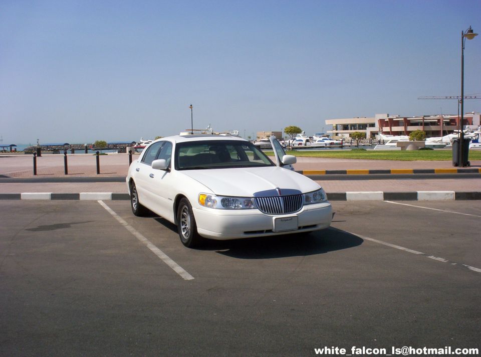 White sedan with driver's door open, parked in a lot with a waterfront in the background