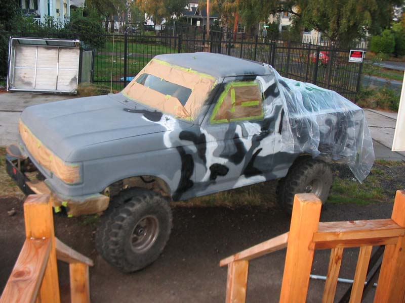 Lifted Ford Bronco in primer being masked and painted camouflage in driveway