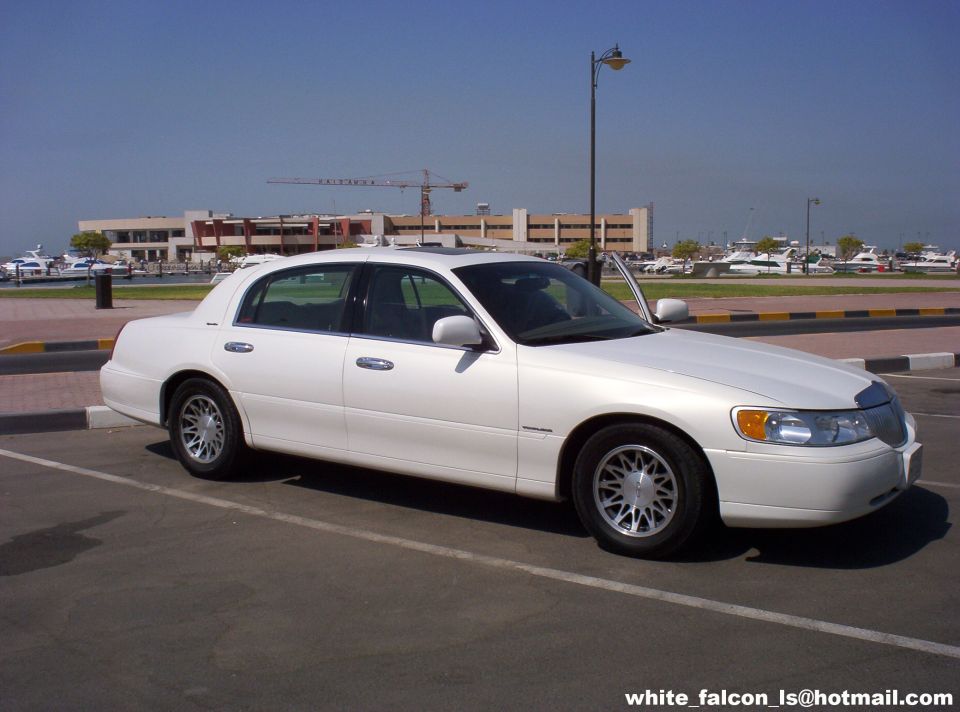 1999 Mercury Grand Marquis parked in a lot with buildings and boats in the background