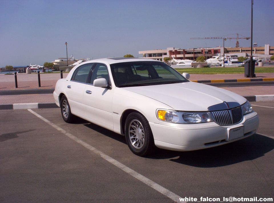 White sedan parked in a lot, front quarter view. Visible grille and headlights