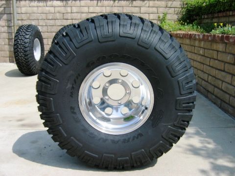 1985 Ford Bronco - Two large off-road tires with chrome rims are displayed outdoors, with a brick wall in the background.