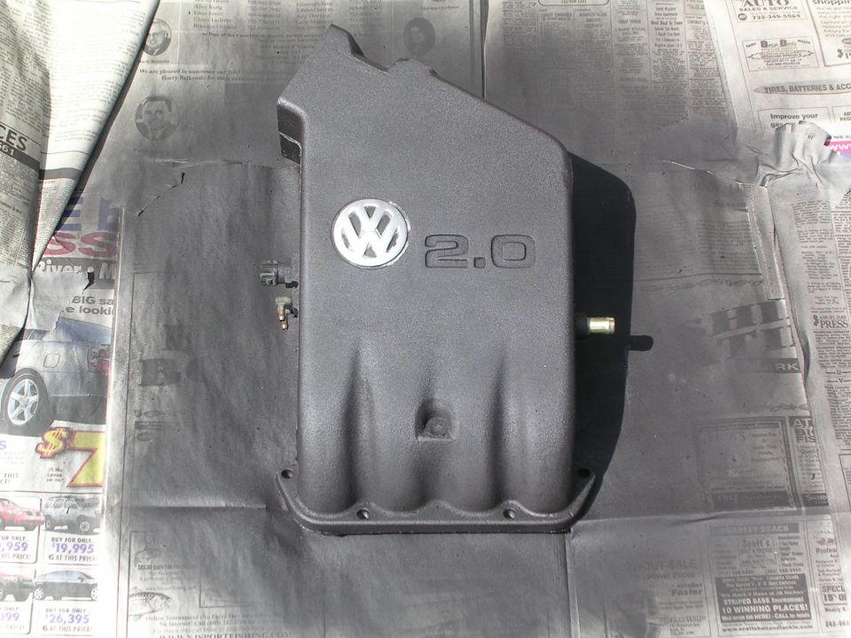 Black-painted VW 2.0 engine intake manifold cover drying on newspaper covered in overspray