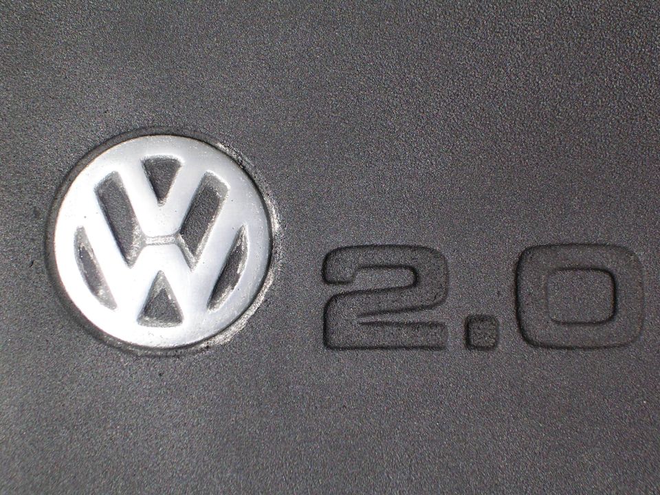 Close-up of Volkswagen roundel logo and embossed '2.0' text on gray plastic engine cover