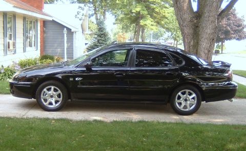 2004 Ford Taurus - A black 2004 Ford Taurus sedan is parked on a driveway in front of a house.