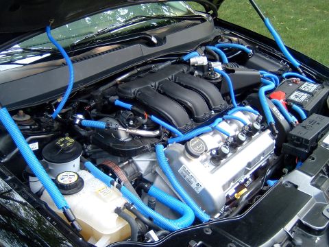 2004 Ford Taurus - Engine bay modified with blue hoses and tubing, showing various engine components and the battery.