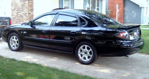 2004 Ford Taurus - A black 2004 Ford Taurus sedan is parked on a driveway in front of a house.