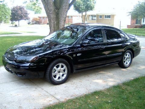 2004 Ford Taurus - A black 2004 Ford Taurus sedan is parked on a driveway in front of a residential home.