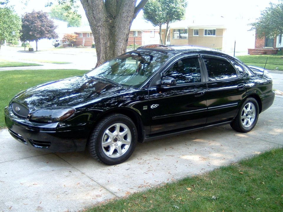 Black Ford Taurus sedan side profile parked on a driveway