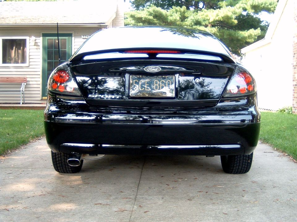 Rear of a black Ford Taurus sedan with spoiler and Michigan plate in a driveway