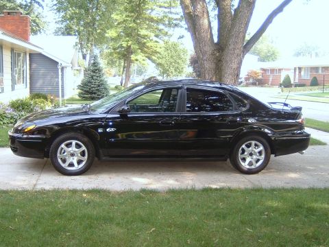 2004 Ford Taurus - Side view of a black 2004 Ford Taurus sedan parked in front of a house.