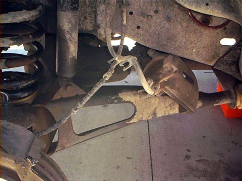 1995 Ford Bronco - Underside view of a Ford Bronco showing front suspension components, including a rusty coil spring, shock absorber, control arm, and a rout…