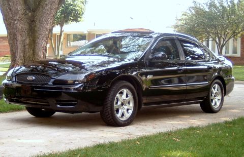 2004 Ford Taurus - A black 2004 Ford Taurus is parked on a concrete driveway in front of a house.