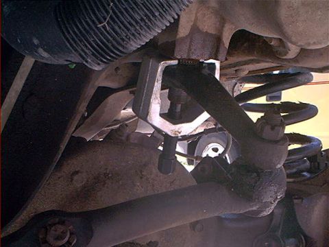 1995 Ford Bronco - Underside view of a front suspension showing a coil spring, control arms, and a threaded tool or coil spring compressor fitted around a sus…