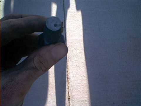 1995 Ford Bronco - A hand holds a short cylindrical metal part, possibly a bushing or spacer, up to the camera in bright sunlight against a light-colored surf…