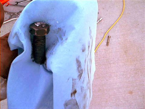 1995 Ford Bronco - A large rusty hex-head bolt with coarse threads rests on a white cloth, likely part of a lift kit component. A yellow wire and small metal…