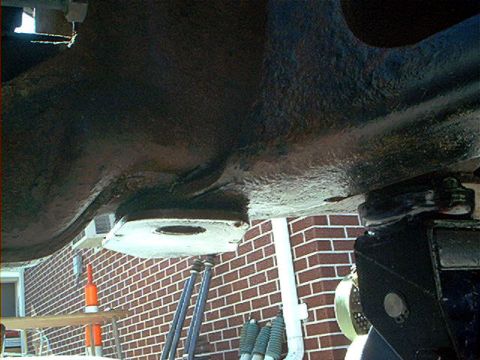 1995 Ford Bronco - Underside view of a vehicle chassis showing a rusty frame rail with a freshly painted white bracket or crossmember, photographed from below…