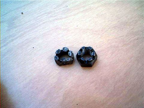 1995 Ford Bronco - Two black castellated (castle) nuts sitting on a plywood surface; the one on the left has badly rounded, chewed-up corners while the right…