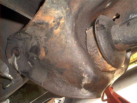 1995 Ford Bronco - Close-up under-vehicle view of a surface-rusted cast differential housing and axle tube, with the pinion snout visible at right and a red j…