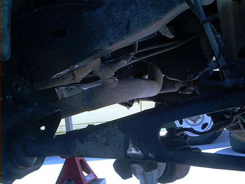 1995 Ford Bronco - Underside view of a vehicle raised on a red jack stand, showing the exhaust pipe, driveline, front axle, differential, and suspension compo…