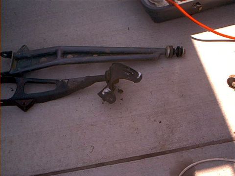 1995 Ford Bronco - Two front suspension radius arms laid side by side on a concrete driveway for comparison, one gray arm fitted with a bushing and washer sta…