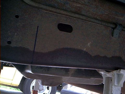 1995 Ford Bronco - Underbody shot looking up at a truck's frame rail and rocker area, showing surface rust, factory punched holes and an oval access slot, wit…