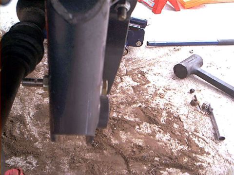1995 Ford Bronco - Ground-level shot under a vehicle mid-suspension-job, looking at a boxed frame rail with a bracket and bolts and a rubber CV/axle boot at l…