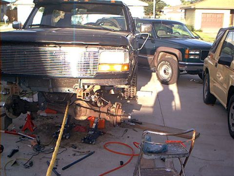 1995 Ford Bronco - A dark Ford truck sits on jack stands in a residential driveway mid-lift install, front bumper and grille removed and the Dana front axle w…