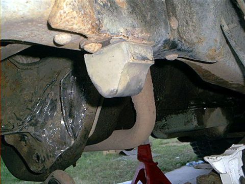 1995 Ford Bronco - Underbody close-up of a light-colored rubber bump stop hanging from a rusty frame bracket above the front axle, with a grease-coated axle h…