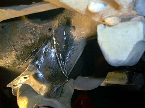 1995 Ford Bronco - Underbody close-up of a stamped-steel bracket or crossmember area showing a bright, freshly ground or welded seam amid heavy grime, with an…