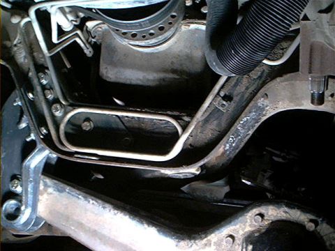 1995 Ford Bronco - Underbody close-up showing steel brake or fuel lines bent with a looped section and secured to a bracket near the transmission crossmember,…