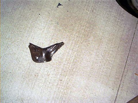 1995 Ford Bronco - A small bent and twisted sheet-metal bracket lying on a light concrete garage floor, folded over on itself with a single bolt hole visible…