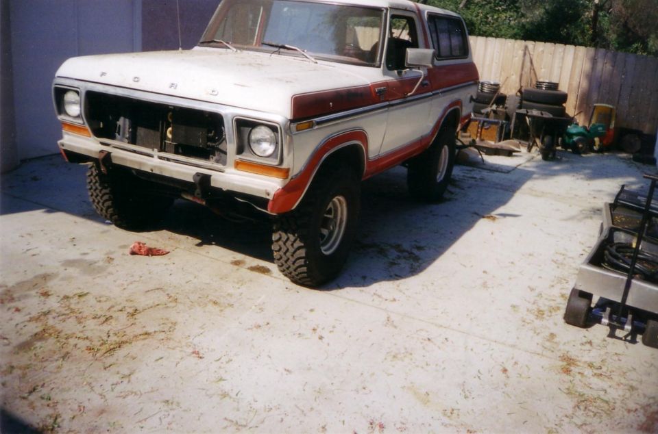 1978 Ford Bronco, white and red, front end missing grille, parked on concrete