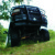 1995 Ford Bronco - A black SUV with off-road tires is parked on a grassy incline, partially obscured by trees.