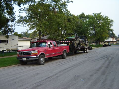 1992 Ford Bronco - Red Ford pickup truck hauls two off-road vehicles on a trailer down a residential street.
