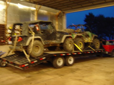 1992 Ford Bronco - Two off-road vehicles are secured to a trailer inside a garage.