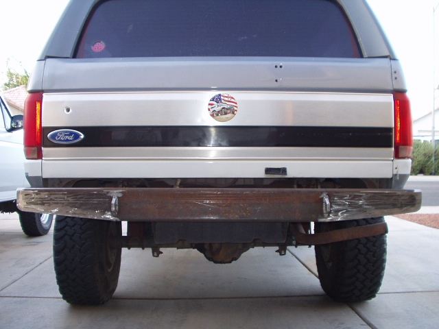 Rear of silver Ford SUV with rusty bumper and off-road tires on driveway