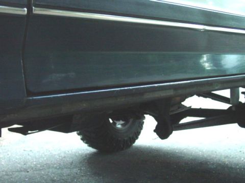 1986 Ford Bronco - Low ground-level view along the passenger-side rocker panel of a dark blue truck, showing the body-side chrome trim strip and the underside…