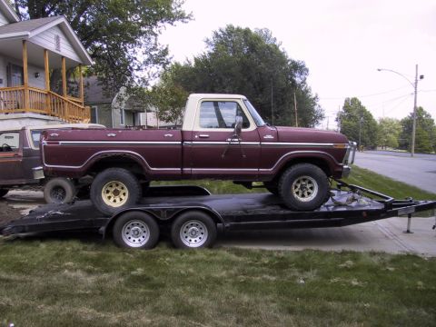 1983 Ford Bronco - A maroon and white pickup truck is loaded onto a trailer, with another vehicle partially visible behind it.