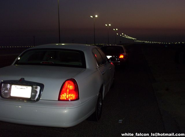 Rear view of a white sedan driving at night, with another car behind it