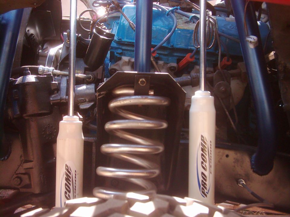 Close-up of engine bay showing blue engine block, Pro Comp shocks, and coil spring
