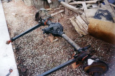 1978 Ford Bronco - Two vehicle axles are shown disassembled and resting on the ground, with one supported by jack stands.