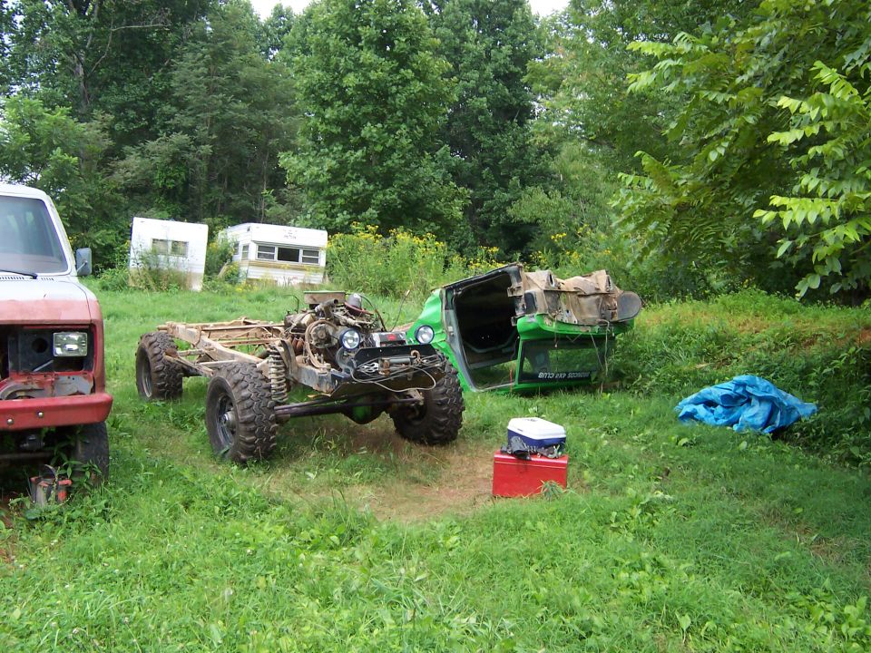 Bronco body tub flipped upside down next to its bare rolling chassis with engine and mud tires in a grassy yard