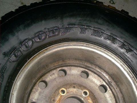 1995 Ford Bronco - Close-up of the raised 'GOODYEAR' lettering on the sidewall of a mounted light-truck tire, laid flat on a concrete floor. The tire sits on…