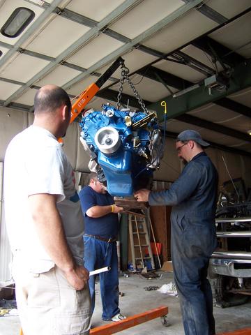 1979 Ford F-150 - Three men work together to install a blue engine using an engine hoist in a garage setting.