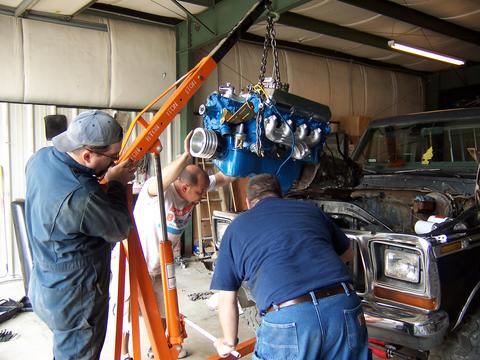 1979 Ford F-150 - Workers are carefully lowering a newly rebuilt engine into the engine bay of a Ford F-150 truck.