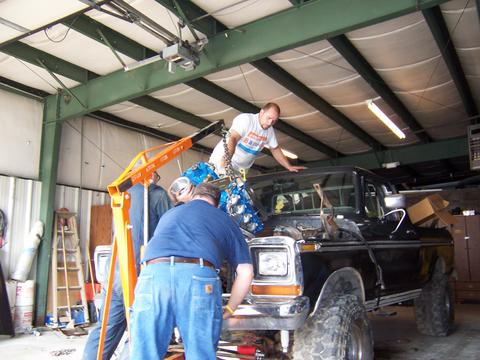 1979 Ford F-150 - Mechanics install an engine into a black pickup truck in a garage.
