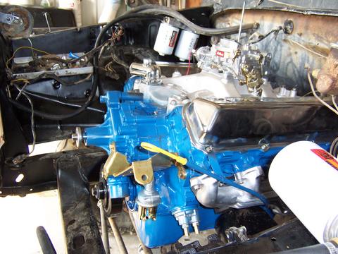 1979 Ford F-150 - Close-up of a blue engine block with chrome valve covers and carburetor, likely during installation.